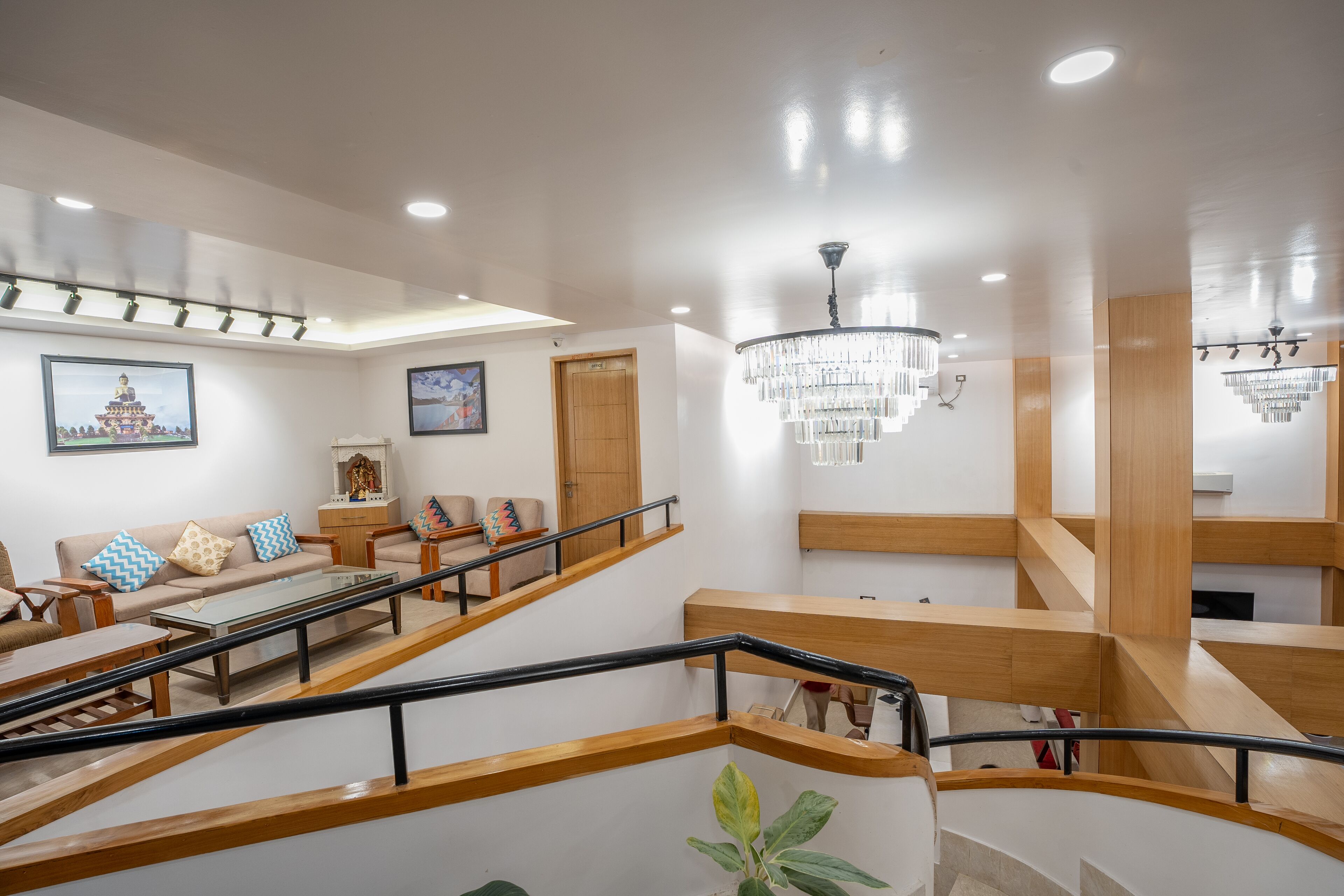 A modern hotel lobby with a staircase, seating area, and chandeliers.
