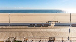 Blick auf einen Strand von einer Holzdielenveranda mit Geländer, einer Bank und einem Laternenpfahl.