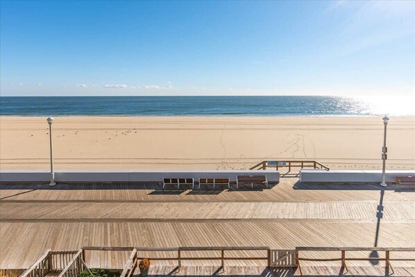 A beach view from a wooden deck with a railing, a bench, and a lamp post. - Oceanfront Three Bedroom Condo on the Boardwalk (Ocean City)