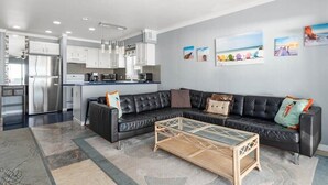 Ein modernes Wohnzimmer mit Ecksofa, Glastisch und Küchenzeile mit Edelstahlgeräten.