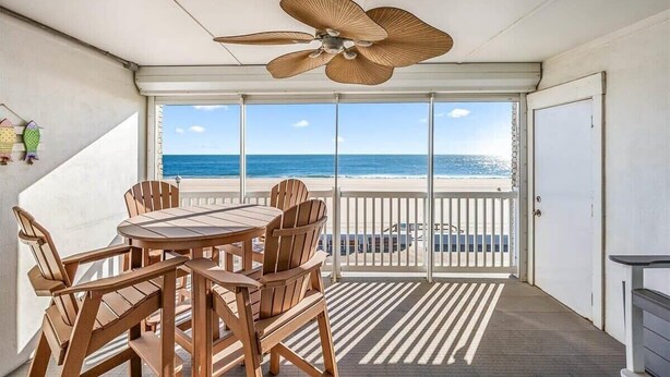 Ein Balkon mit Tisch und Stühlen, einem Deckenventilator und Blick auf den Strand.