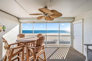 Un balcón con mesa y sillas, un ventilador de techo y vista al mar.