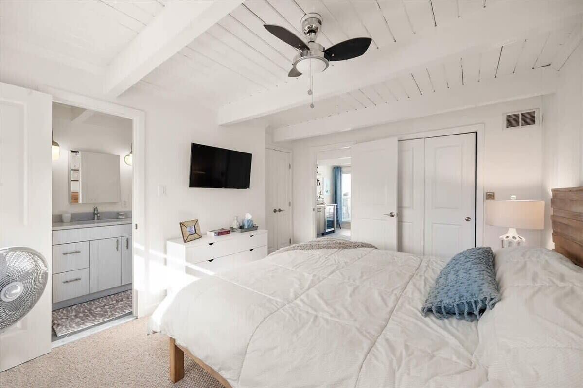 A bedroom with a bed, a ceiling fan, a TV, and a dresser.