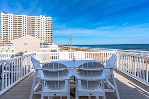 Una terrazza con due poltrone Adirondack bianche e un tavolo, con vista su una spiaggia e un grattacielo sullo sfondo.