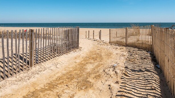 A sandy beach path leading to the ocean, bordered by wooden fences and barbed wire. - Three Bedroom Oceanside Condo Steps from the Beach (Ocean City)