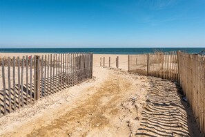 A sandy beach path leading to the ocean, bordered by wooden fences and barbed wire.