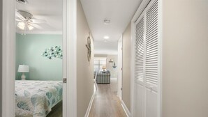 A hallway with a bed, a lamp, a ceiling fan, and a door leading to another room. - Three Bedroom Oceanside Condo Steps from the Beach (Ocean City)