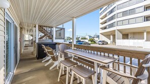 A covered outdoor seating area with wooden furniture, a staircase, and a view of a multi-story building. - Three Bedroom Oceanside Condo Steps from the Beach (Ocean City)