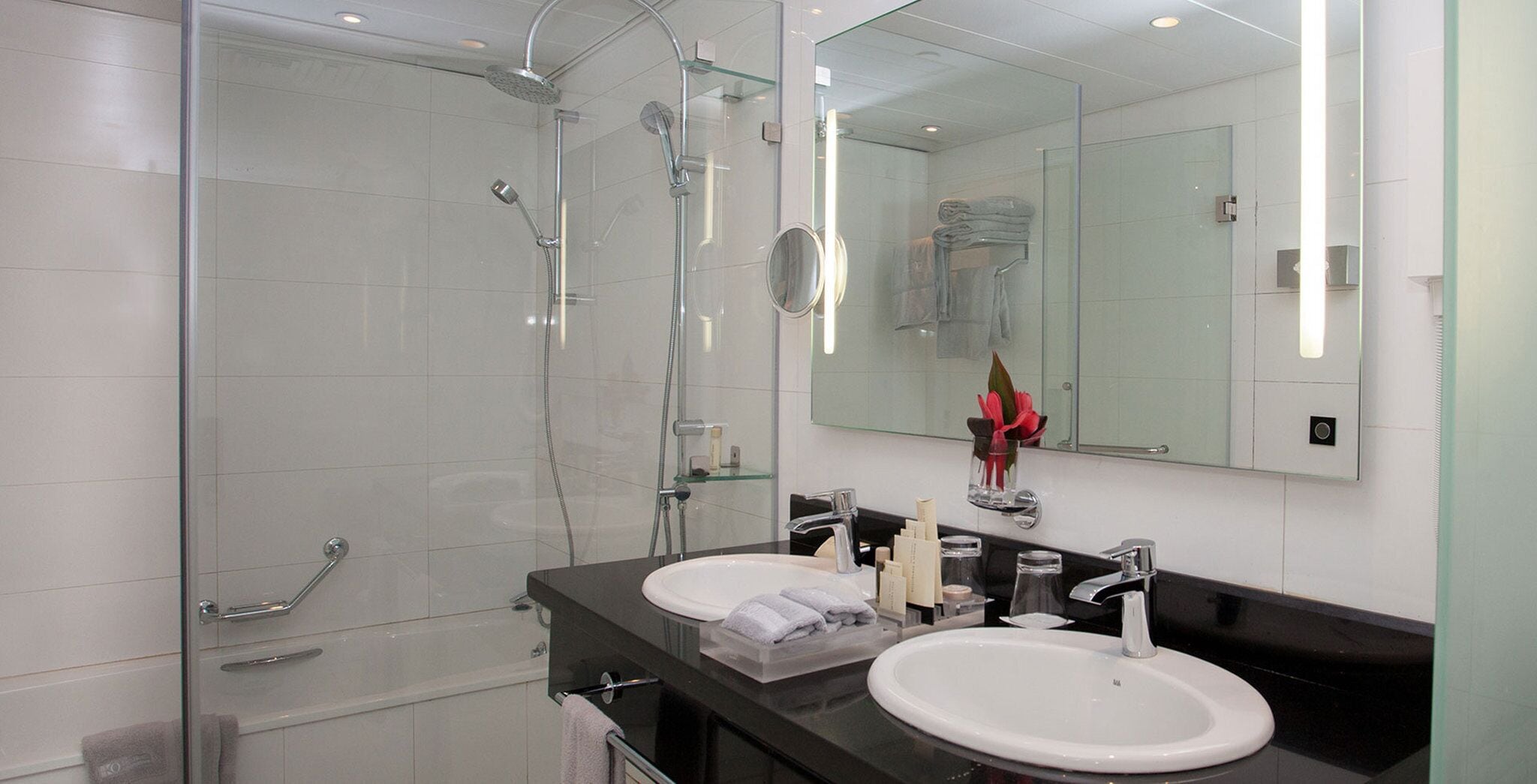 Un baño moderno con dos lavamanos, cabina de ducha de vidrio y un espejo grande.