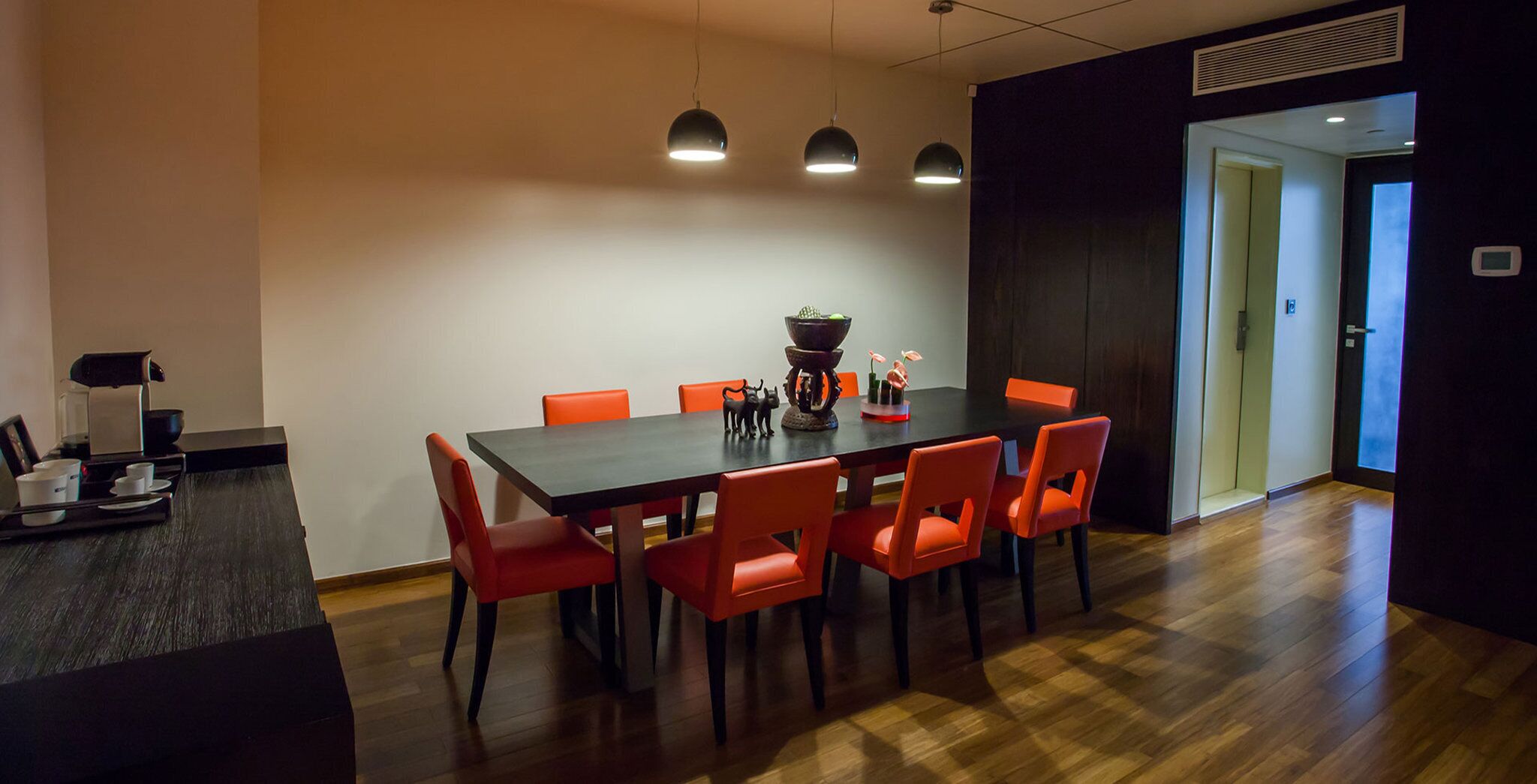 A modern dining area with a dark wooden table, red chairs, and pendant lighting.