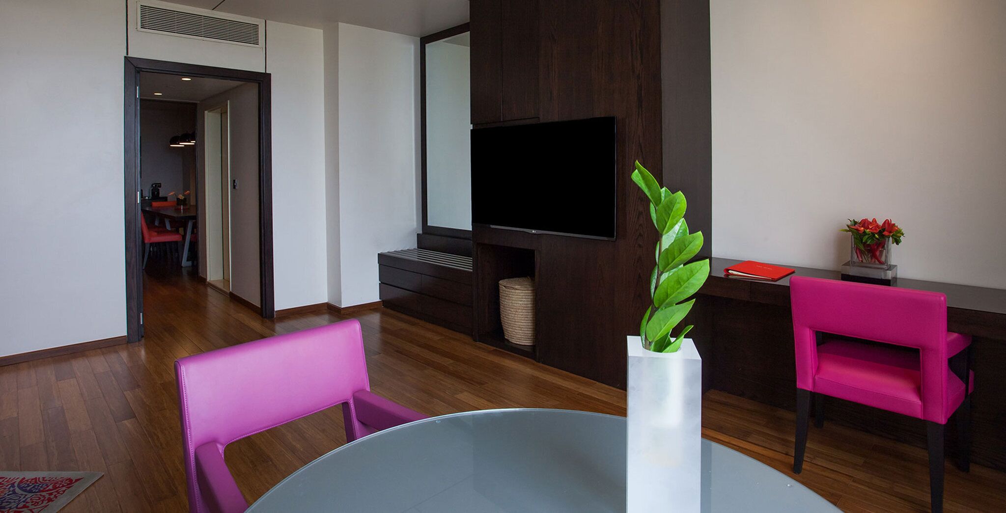 A modern living room with a flat-screen TV, a round table, and two pink chairs.