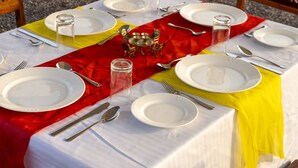 Mesa servida para comer con platos blancos, cubiertos y un camino de mesa rojo.