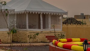 Una carpa blanca con una mesa y sillas, rodeada por un muro de ladrillo bajo y un banco rojo y amarillo.
