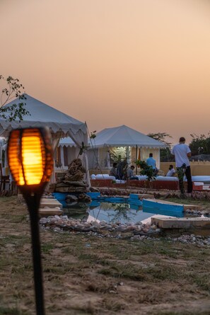 Un camping con tiendas de campaña, un pequeño estanque y gente relajándose.