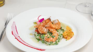Um prato branco com camarões, vegetais, um garfo e um copo de vinho sobre uma mesa.