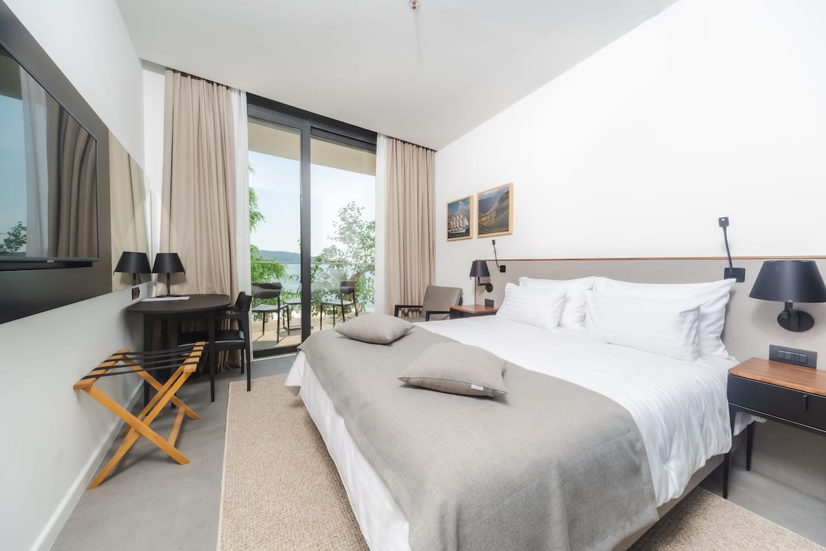 A modern hotel room with a large bed, a desk, and a balcony with a view.