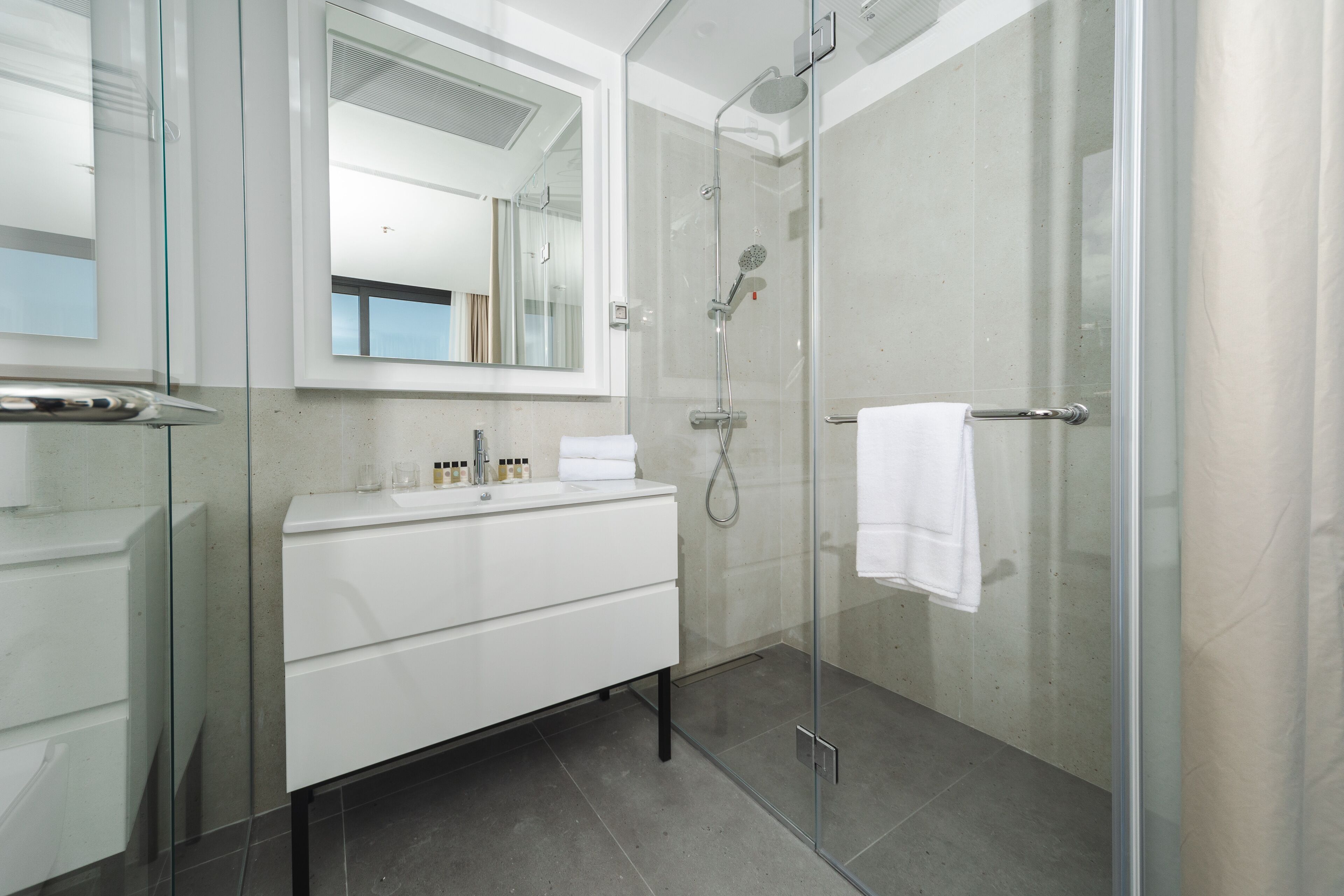 A modern bathroom with a glass shower enclosure, a white vanity, and a large mirror.