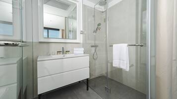 Un baño moderno con cabina de ducha de vidrio, tocador blanco y un espejo grande.