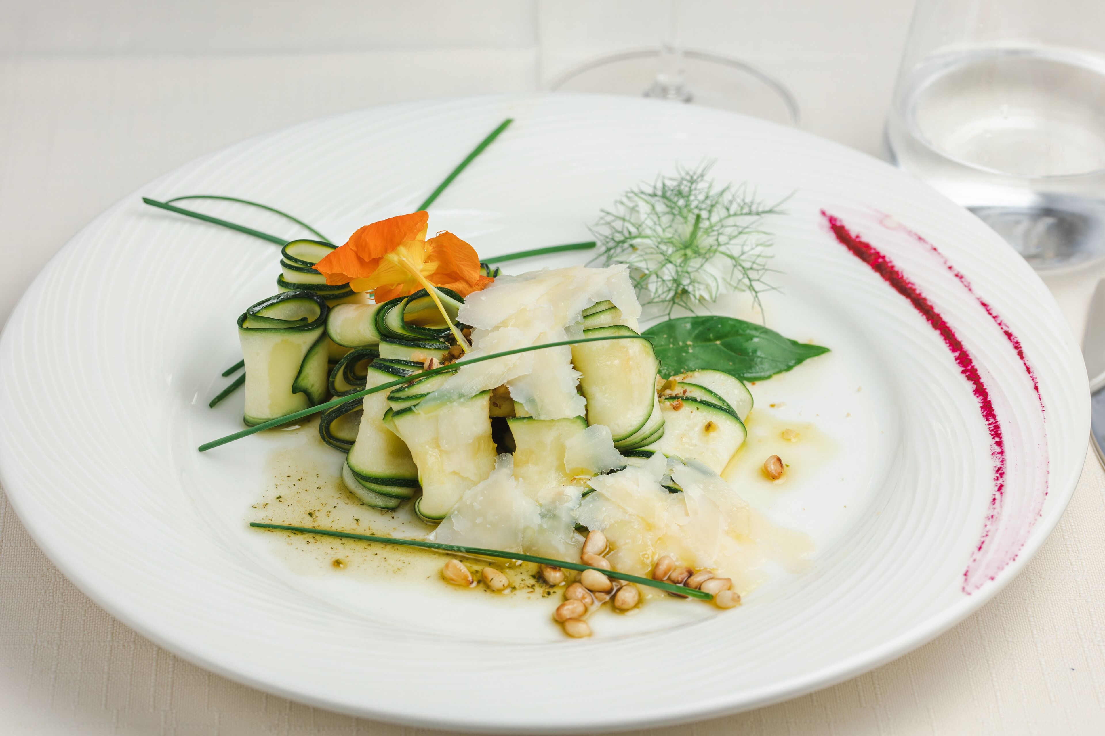 Un piatto bianco con un piatto di pesce, guarnito con erbe aromatiche e un fiore.