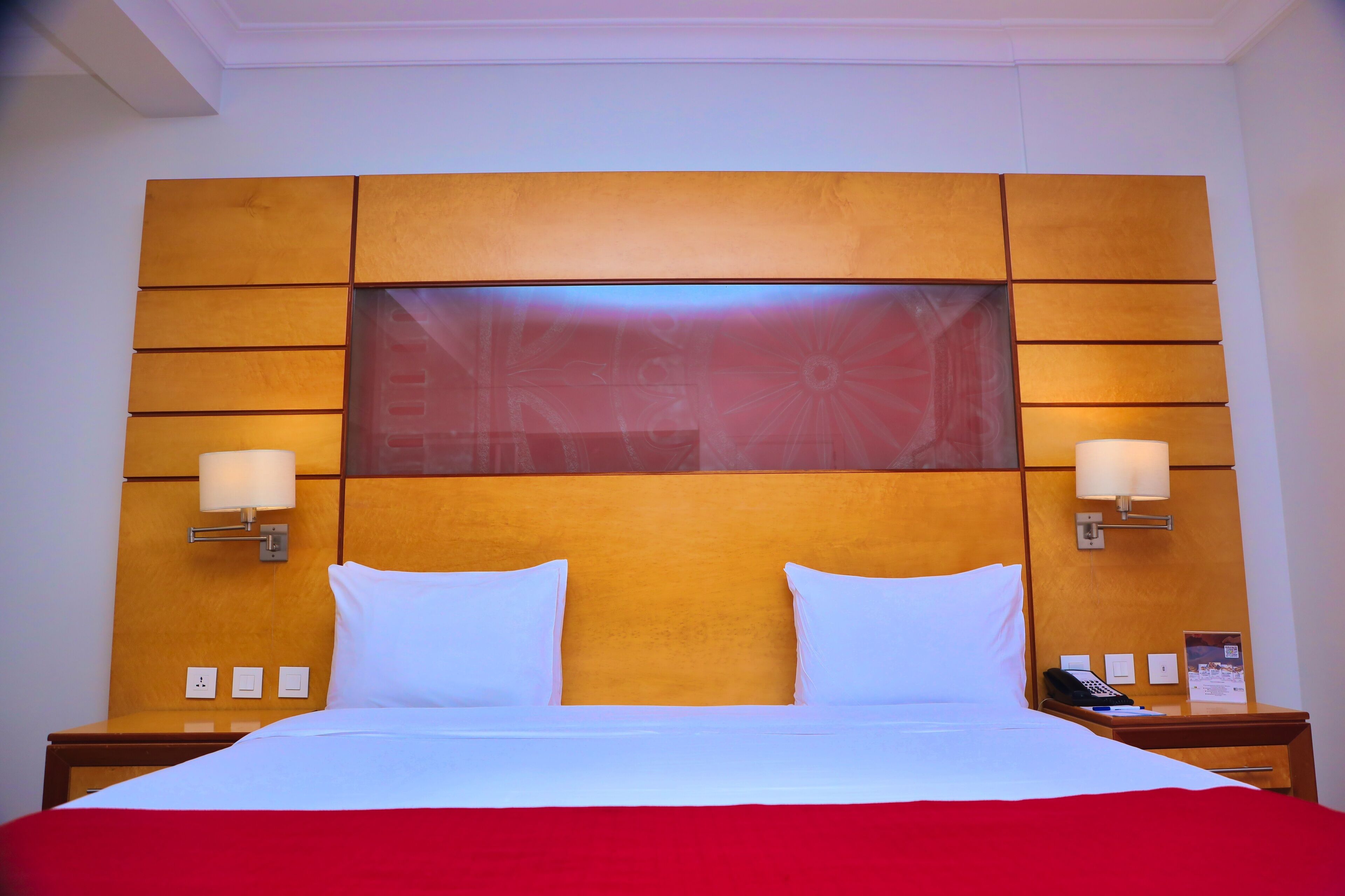 Una habitación de hotel con una cama grande, dos lámparas de noche, una mesita de noche y un panel de control en la pared.