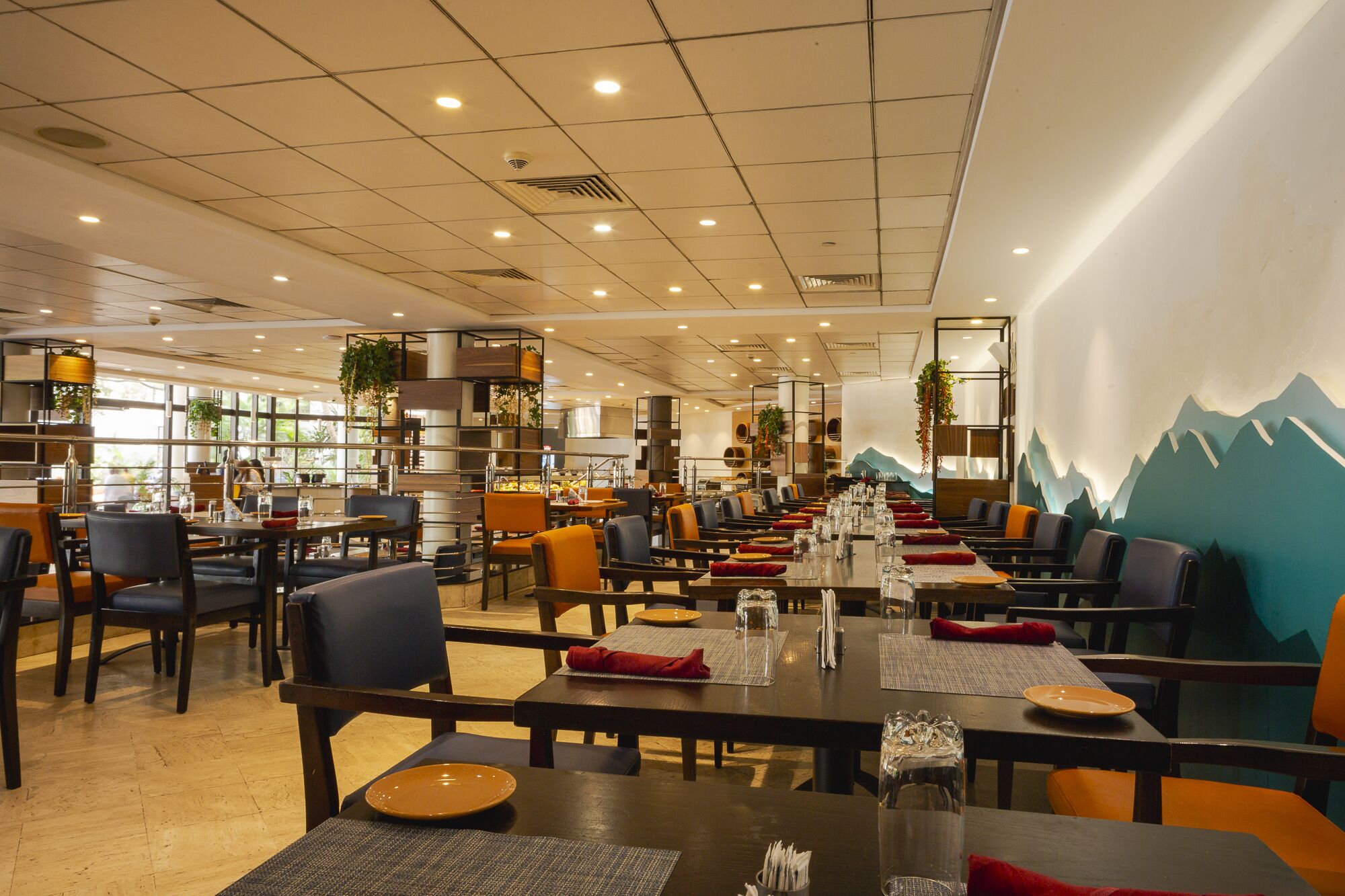 Un restaurante amplio con múltiples mesas y sillas, un diseño de techo moderno y un mural temático de montañas.