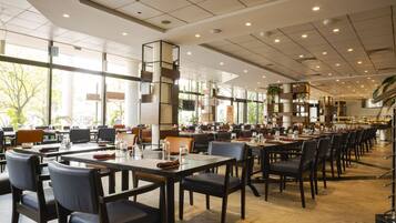 A spacious restaurant with long tables and chairs, large windows, and a modern interior design.