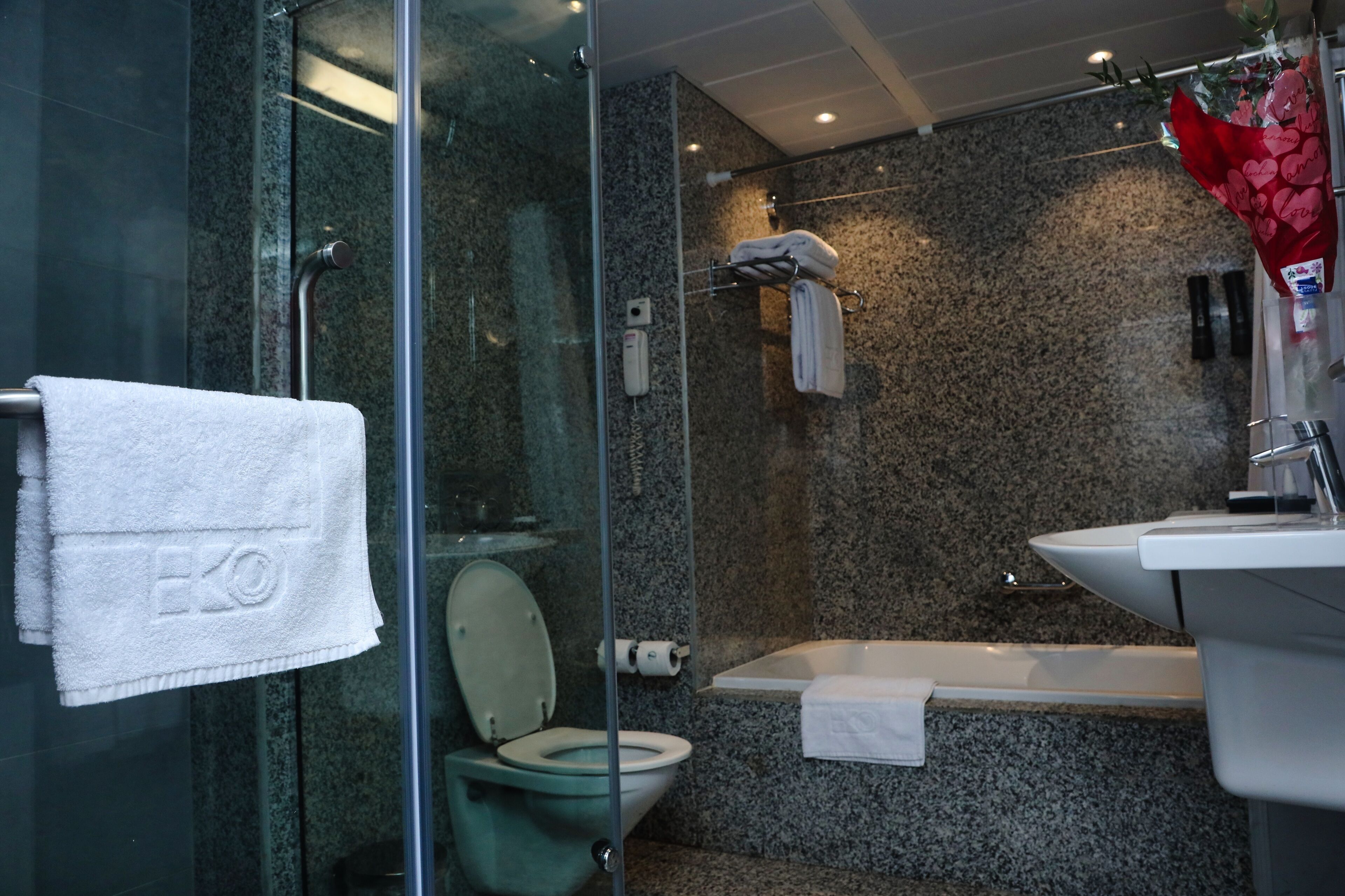 A modern bathroom with a glass-enclosed shower, a toilet with a green seat, a bathtub, and a sink.