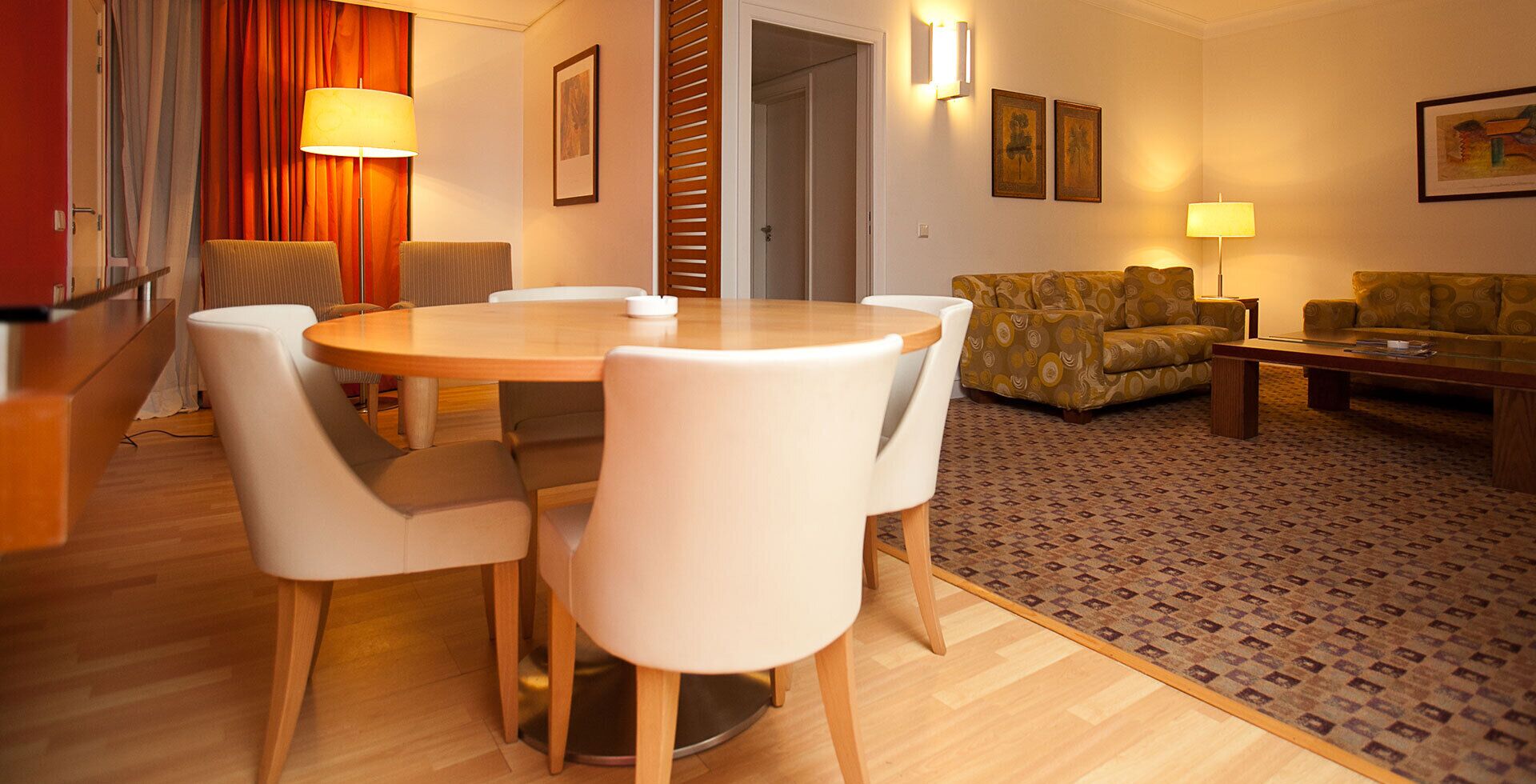 A hotel room with a dining table, chairs, a sofa, a patterned rug, and a wooden floor.
