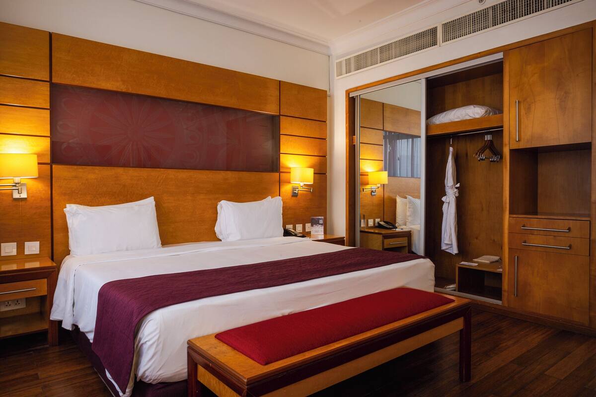 A hotel room with a large bed, bedside lamps, a wardrobe, and a mirror.