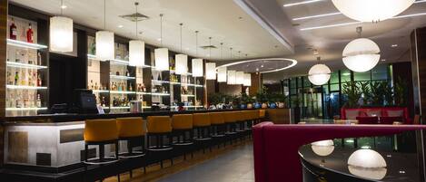 A modern bar area with a long counter, multiple hanging pendant lights, and a seating area with red upholstered chairs.