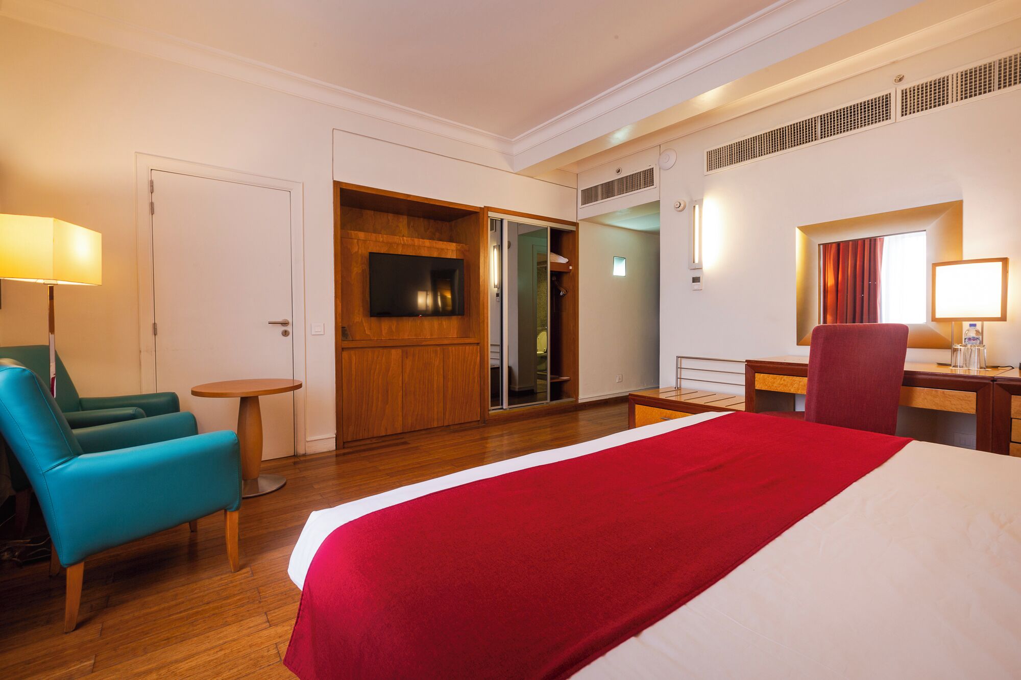 A hotel room with a bed, a desk, a chair, a TV, and a bathroom.