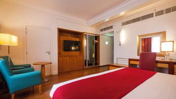 A hotel room with a bed, a desk, a chair, a TV, and a bathroom.