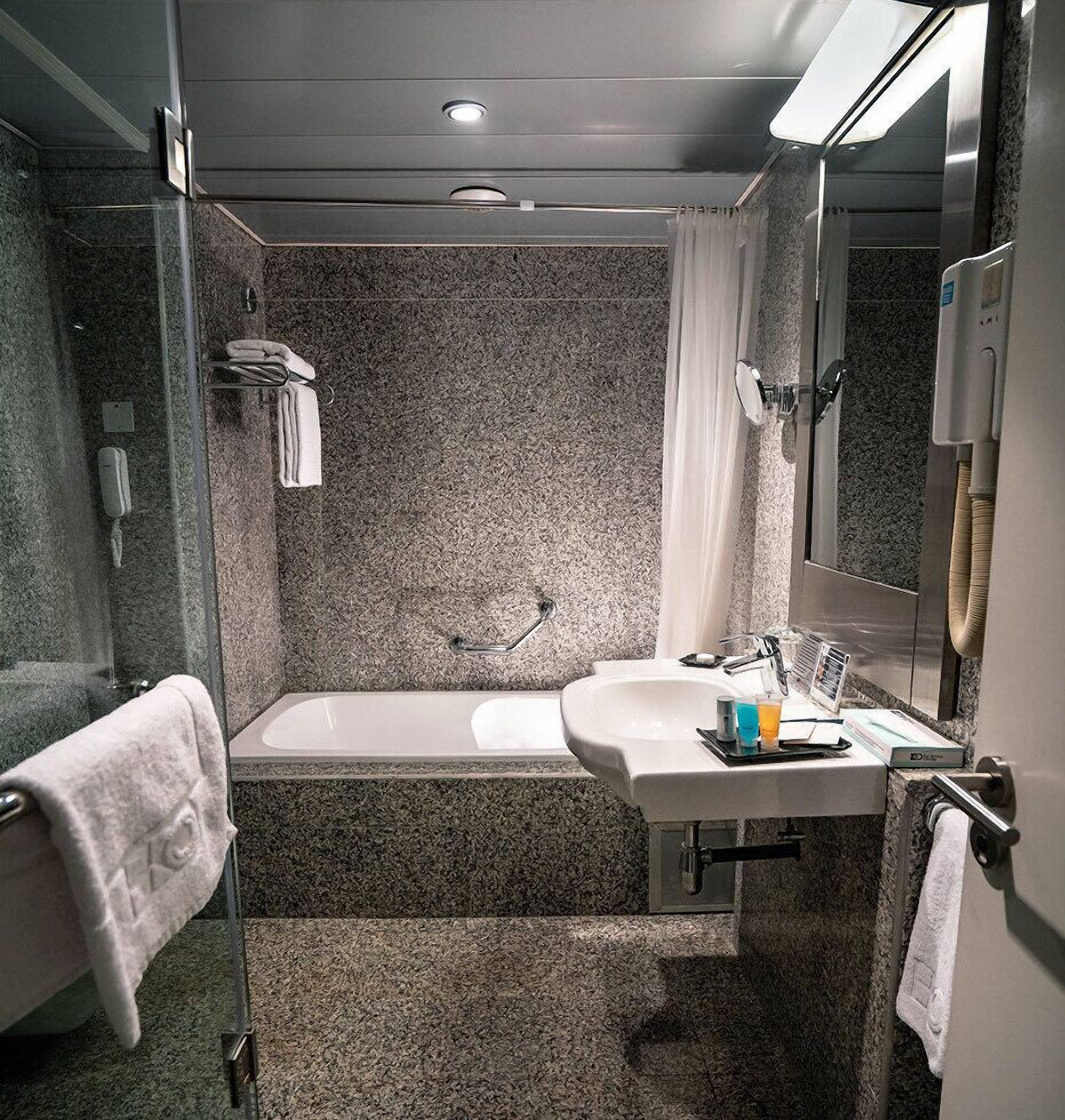 Ein modernes Badezimmer mit einer Glaskabine zur Dusche, einer freistehenden Badewanne und einem Waschtisch mit Waschbecken und Spiegel.
