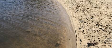 Uma praia arenosa com águas cristalinas, uma pessoa pescando e uma floresta ao fundo.