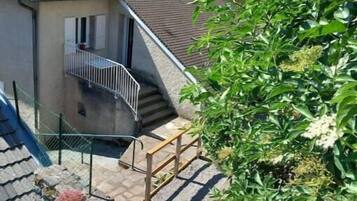 A residential building with a sloped roof, a balcony, and a small outdoor area with steps leading to the entrance.