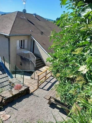 A residential building with a sloped roof, a balcony, and a small outdoor area with steps leading to the entrance. - "l'abri" Confortable et Accueillant (Saint-Front)