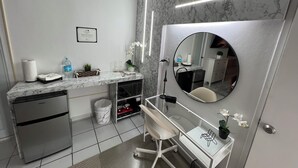 A modern bathroom with a marble countertop, a sink, a mirror, a toilet, and a desk with a chair.