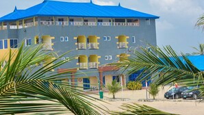 Ein mehrstöckiges Hotel mit Balkonen, einem blauen Dach und einer Sandfläche mit Palmen.