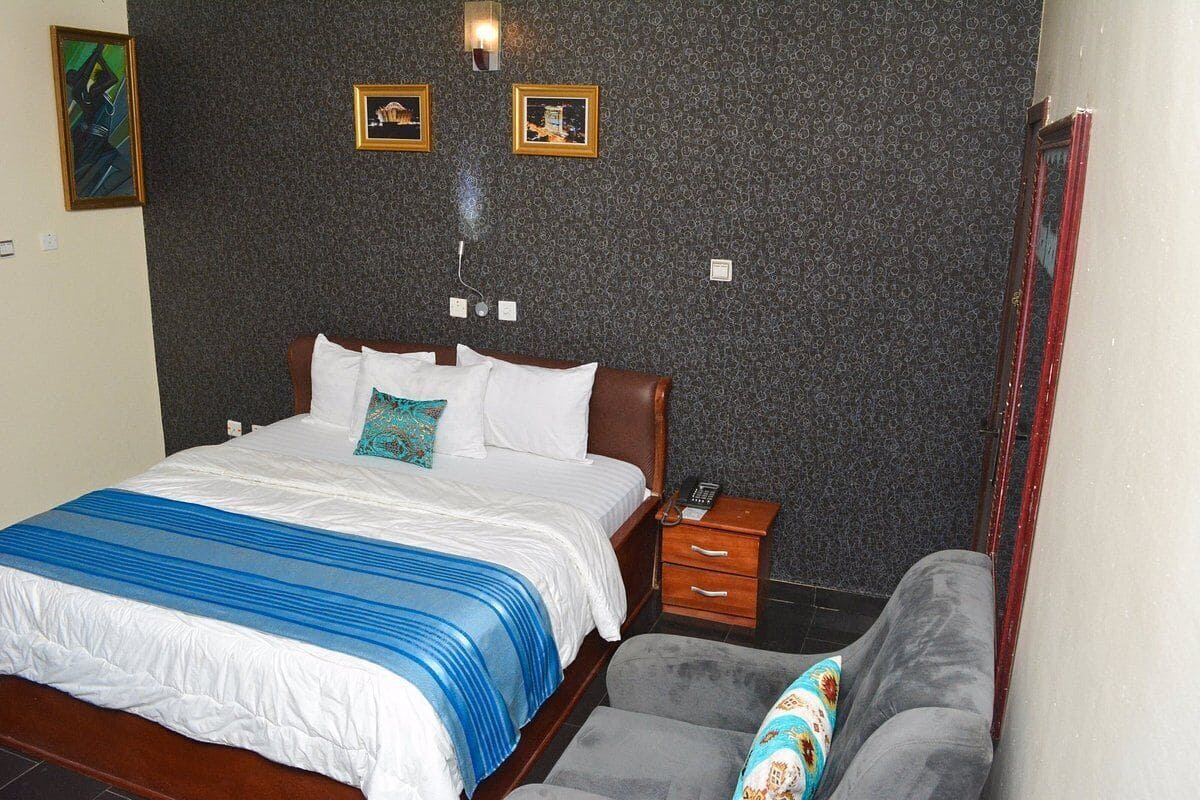 A bedroom with a bed, bedside table, and a grey couch.