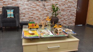 Ein Zimmer mit einem Glastisch, der mit Kinderspielzeug und Büchern, einer Topfpflanze und einer Ziegelwand dekoriert ist.