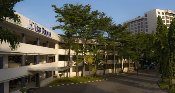 Um hotel com design moderno, apresentando uma estrutura em vários andares com varandas e um pátio central com árvores.