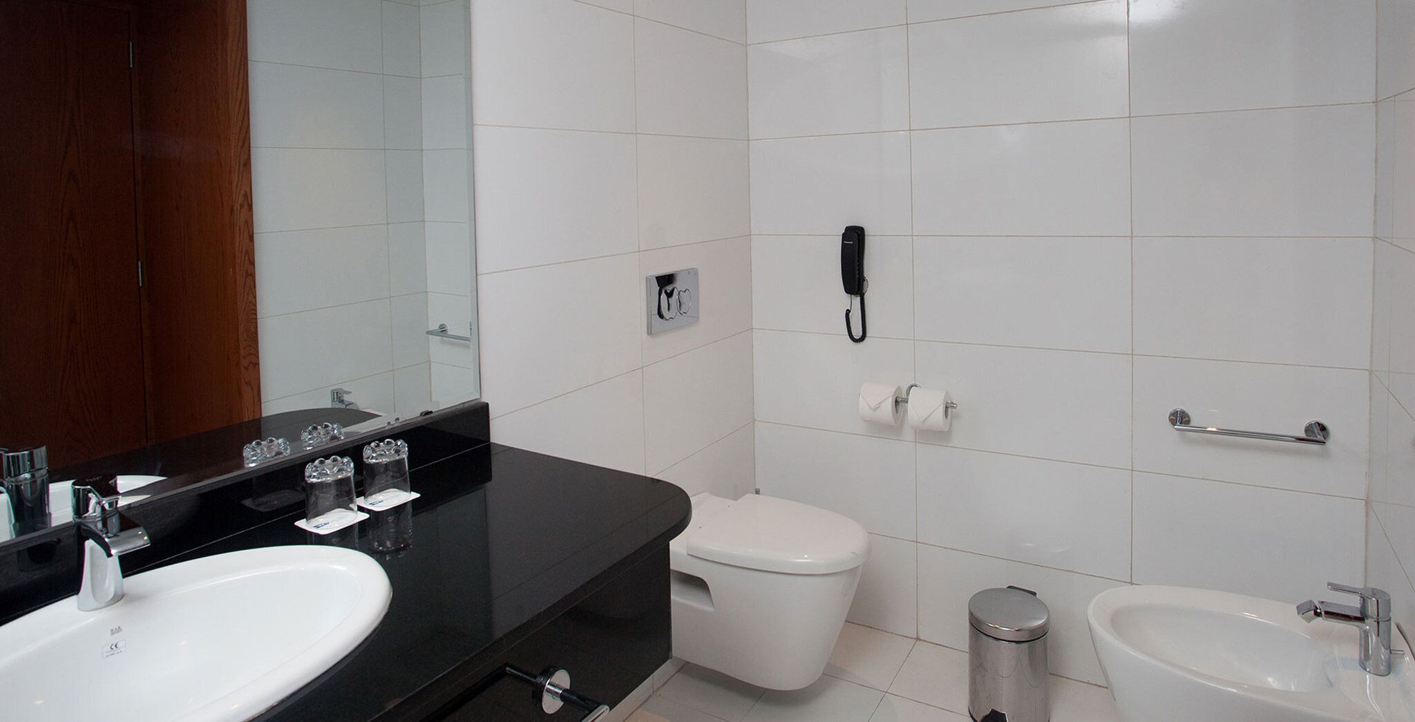 Une salle de bain moderne avec un plan de toilette noir, deux vasques, des toilettes et une poubelle.