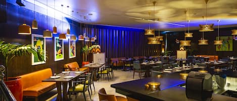 A modern restaurant with multiple dining areas, including a bar and seating with tables and chairs.