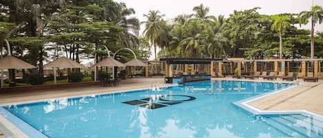 A swimming pool with lounge chairs and umbrellas, surrounded by palm trees.