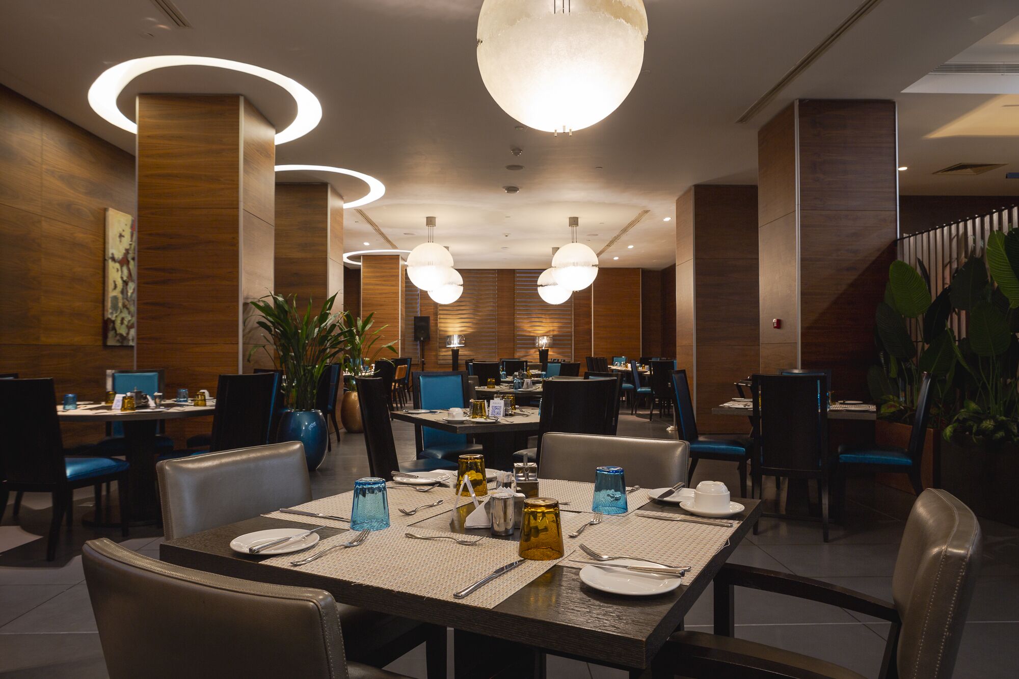 A modern dining area with circular ceiling lights, wooden panel walls, and blue upholstered chairs.