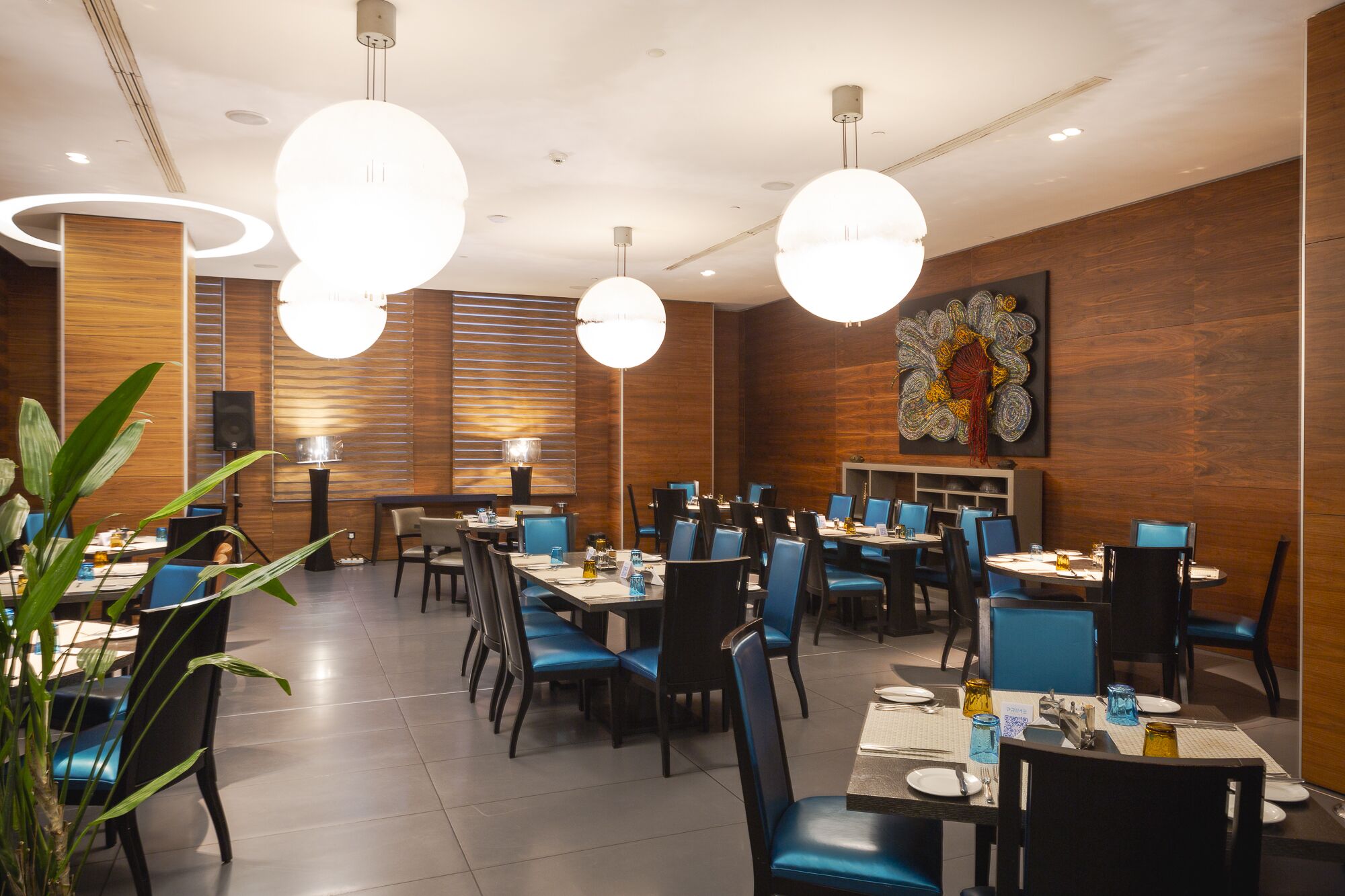 A modern dining area with round tables, blue chairs, and pendant lighting.