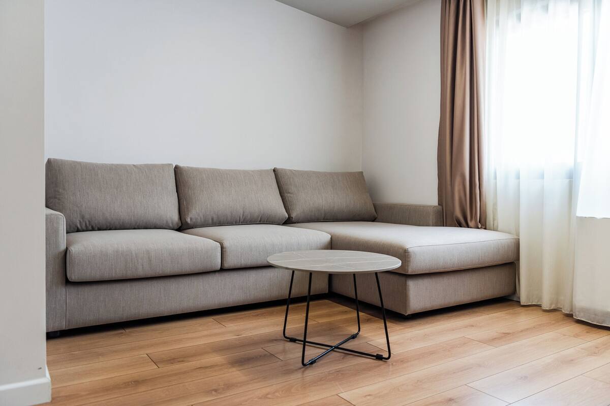 A modern living room with a grey sectional sofa, a small round table, and wooden flooring.