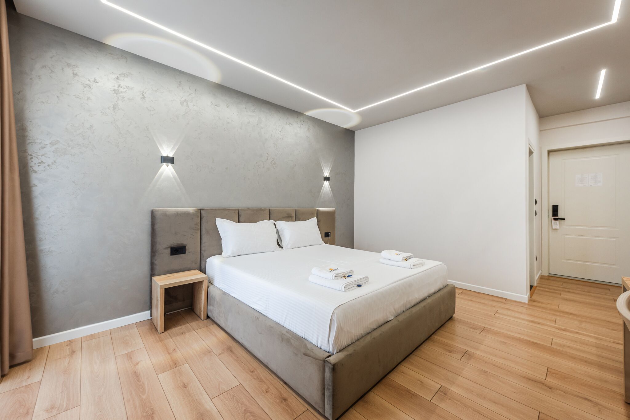 Quarto moderno com cama, luminárias de cabeceira, mesa de cabeceira e piso de madeira.