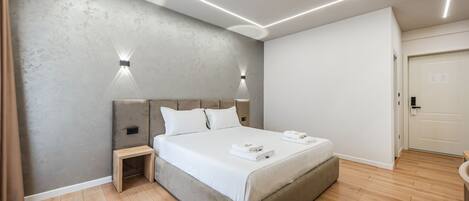 Quarto moderno com cama, luminárias de cabeceira, mesa de cabeceira e piso de madeira.