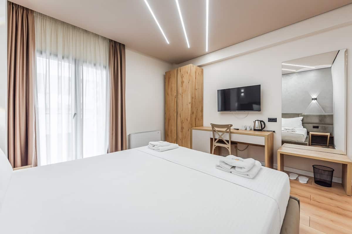 A modern hotel room with a large bed, a desk, a chair, a television, and a mirror.